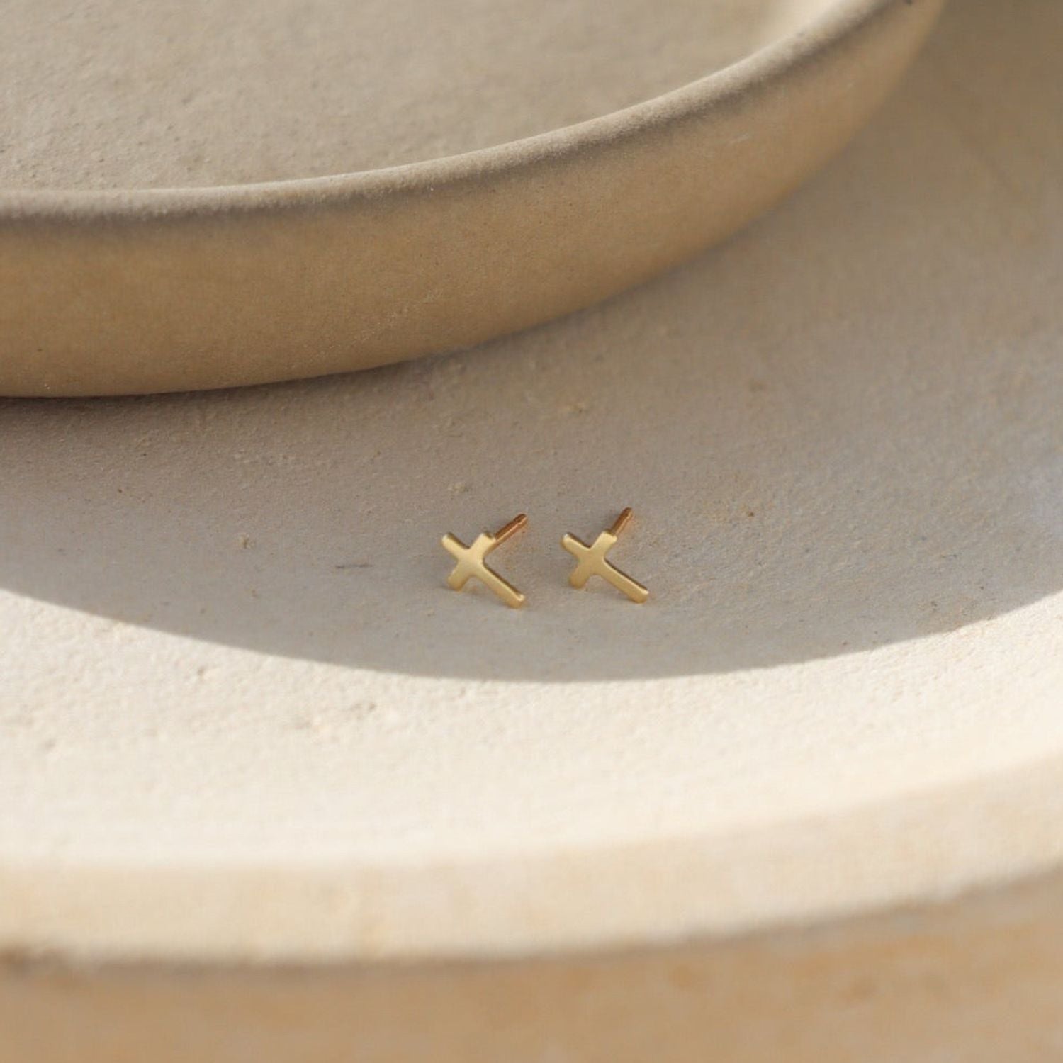 14k gold fill cross shaped studs on a light dish
