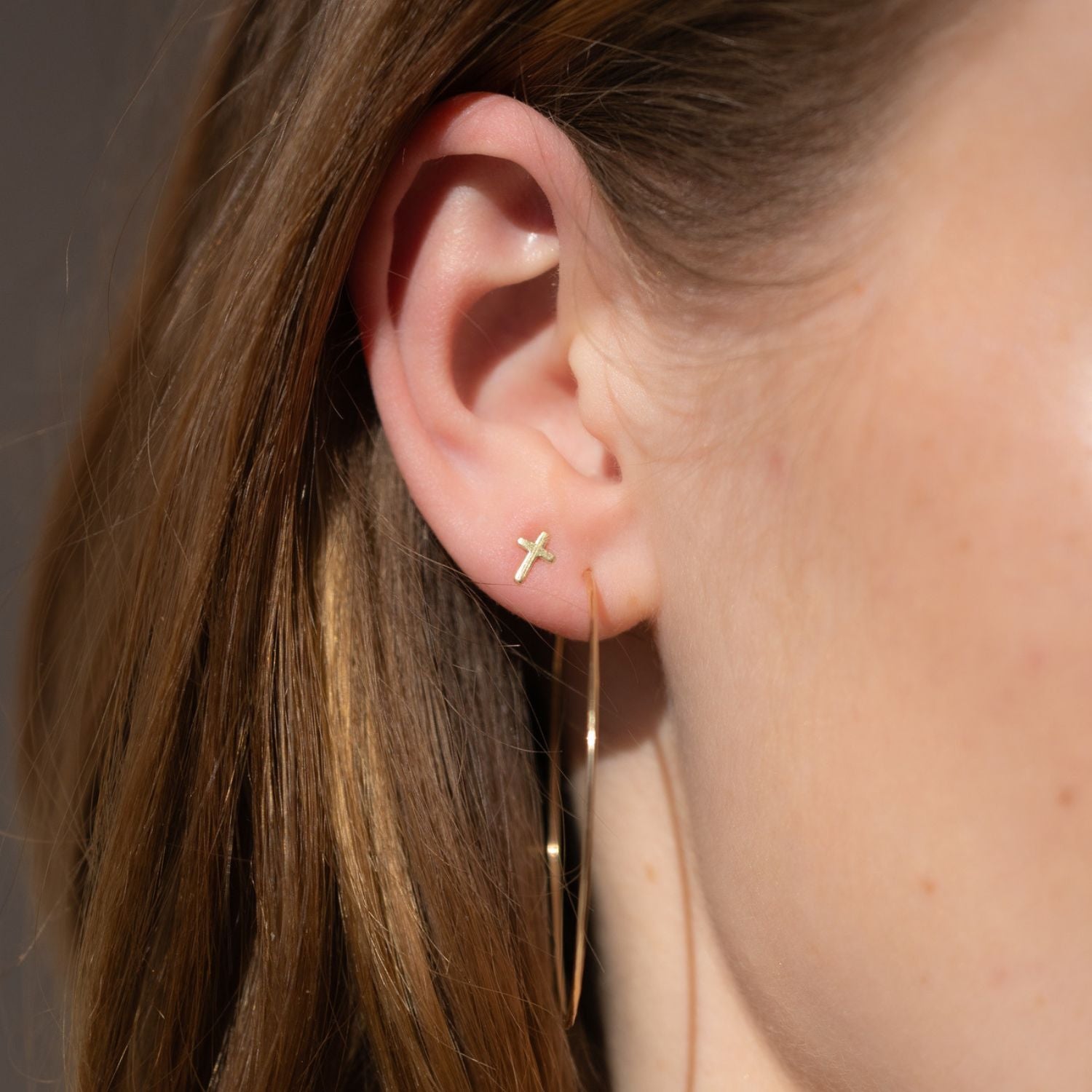 model wearing 14k gold fill cross stud earrings with thin hammered hoops in the sunlight