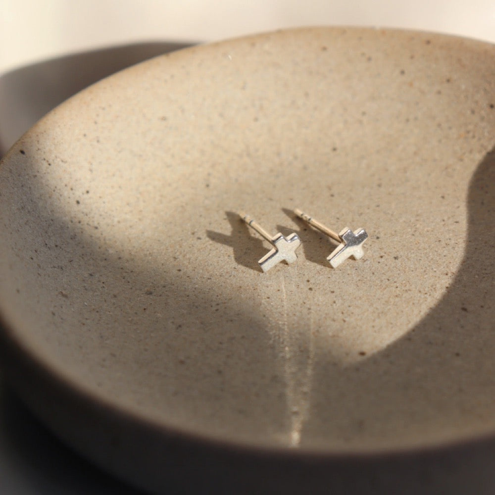 Sterling Silver cross stud earrings. Sitting on a gray plate sitting in the sunlight.