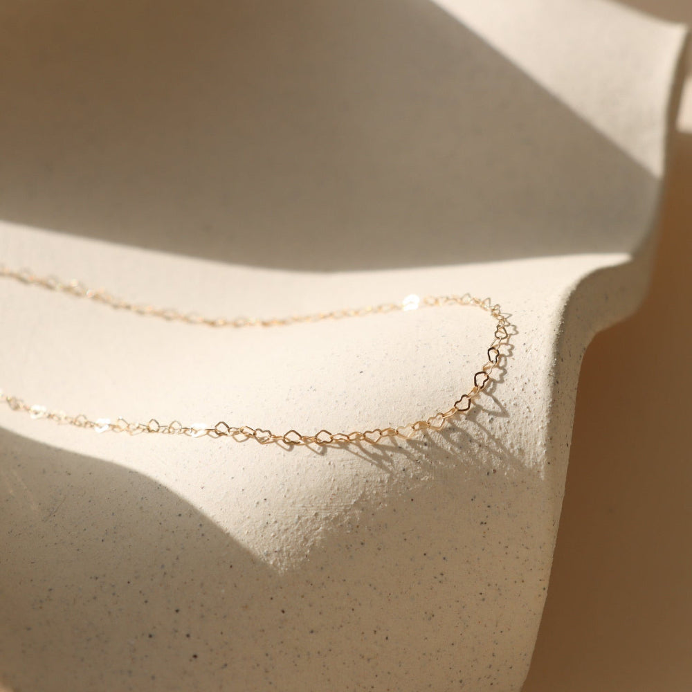 Gold filled dainty heart linked chain necklace on a textured beige surface