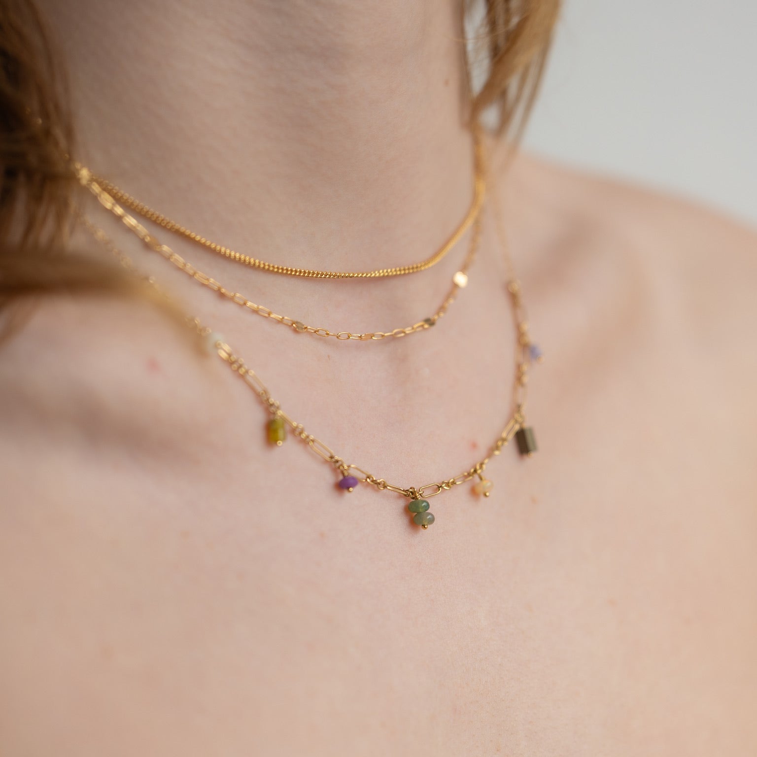 model wearing 14k gold fill chain necklaces paired with a charm necklace with various gemstones