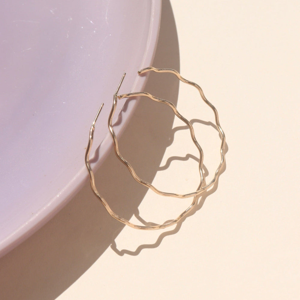 14k gold fill hoop with wave-like textured wire, displayed on a cream backdrop in natural sunlight
