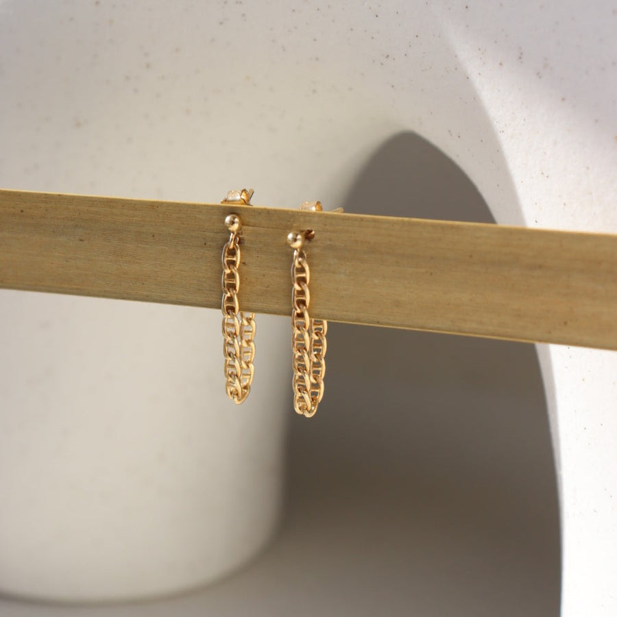 14k gold gill hali chain studs hanging from a plant leaf.