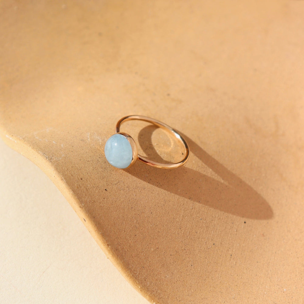 A 14k gold fill hammered gold band with a 8mm aquamarine gemstone set in a gold bezel. The ring is displayed on a orange dish. 
