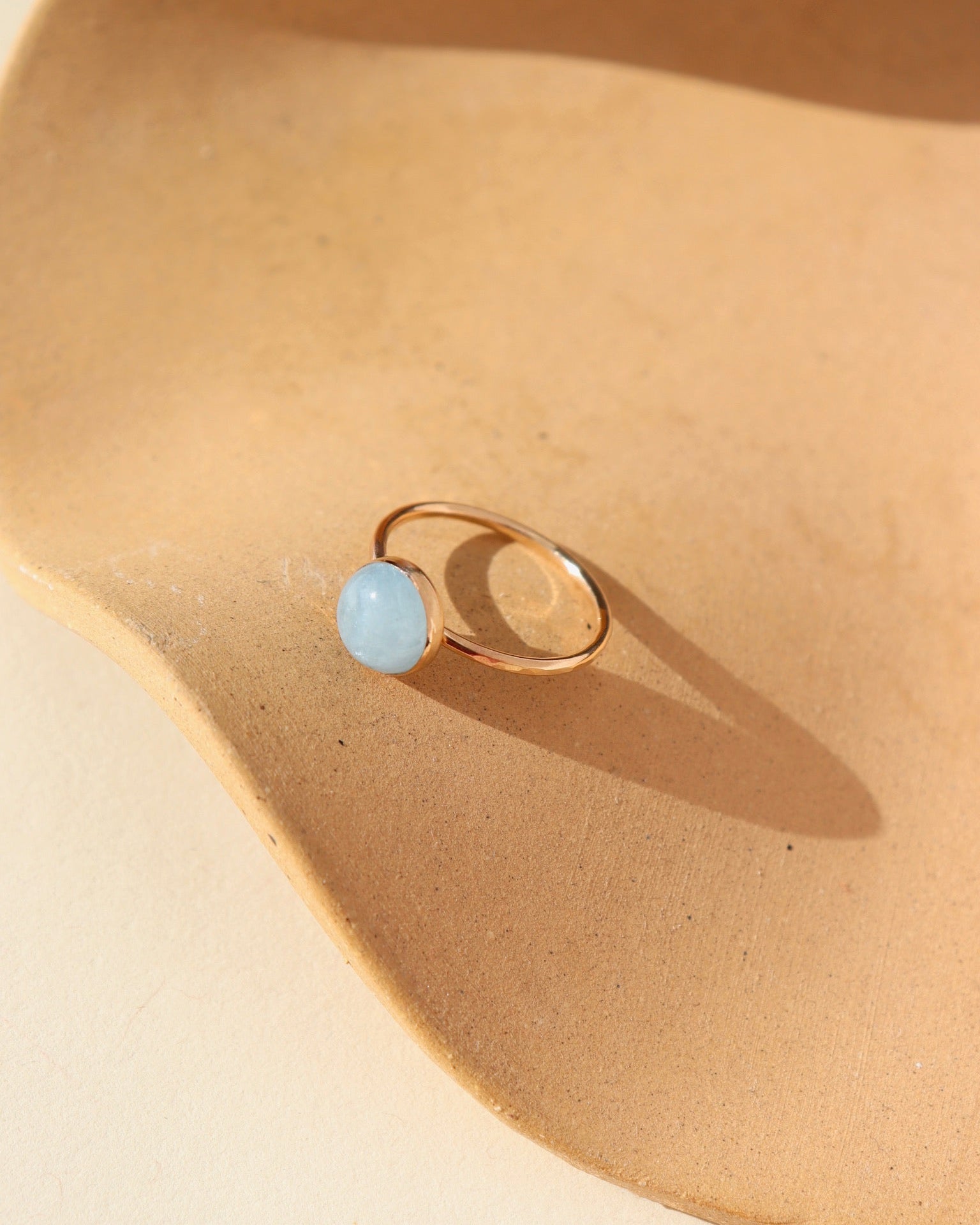 A 14k gold fill hammered gold band with a 8mm aquamarine gemstone set in a gold bezel. The ring is displayed on a orange dish. 