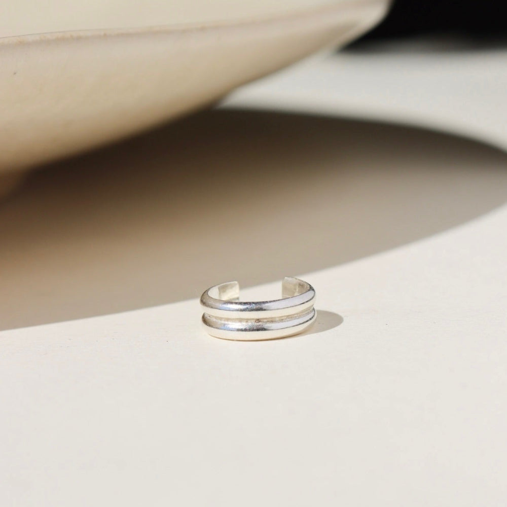 A sterling silver double layered ear cuff, displayed on a cream back drop in the sunlight 