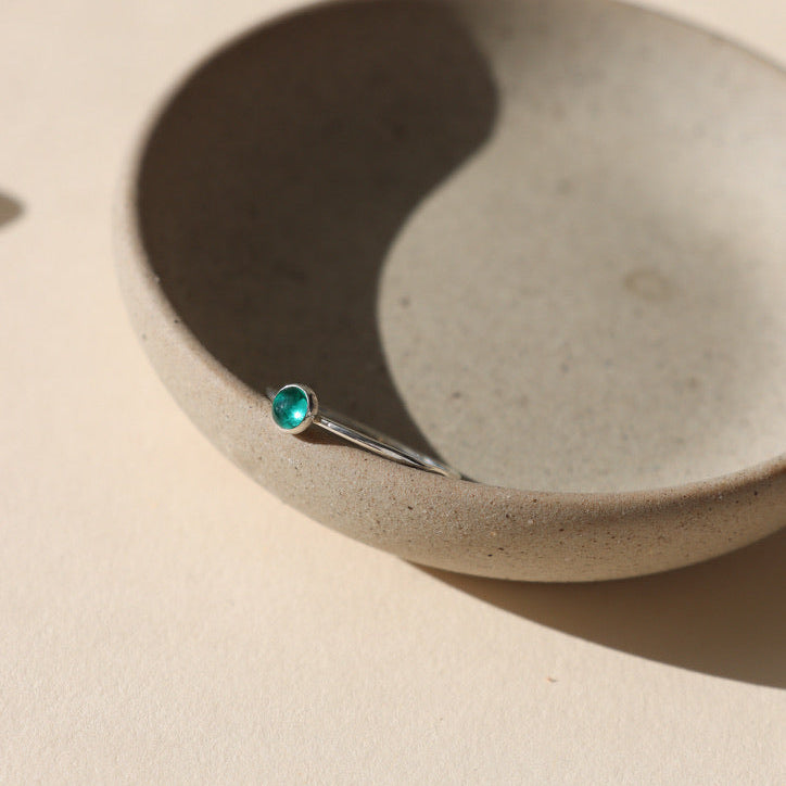 sterling silver band ring with 4mm emerald stone on a light dish