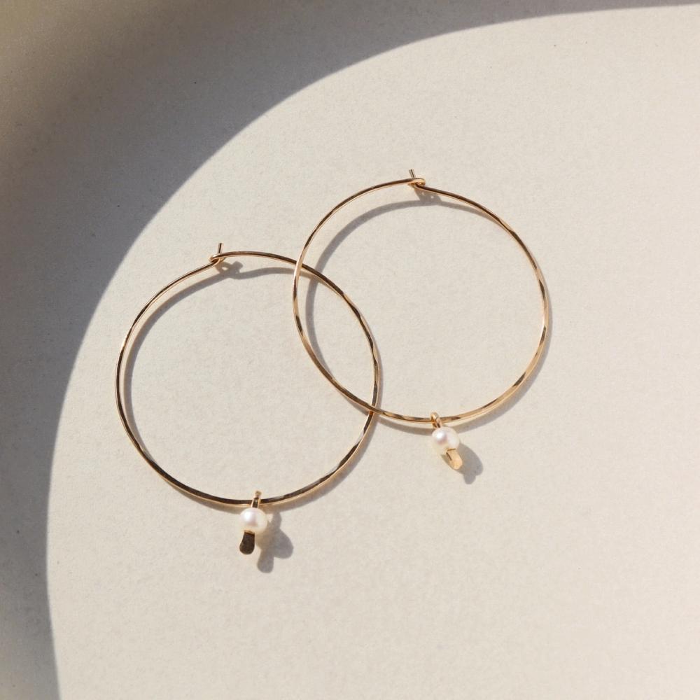 14k gold fill Emma pearl hoops laid on a ceramic plate in the sunlight