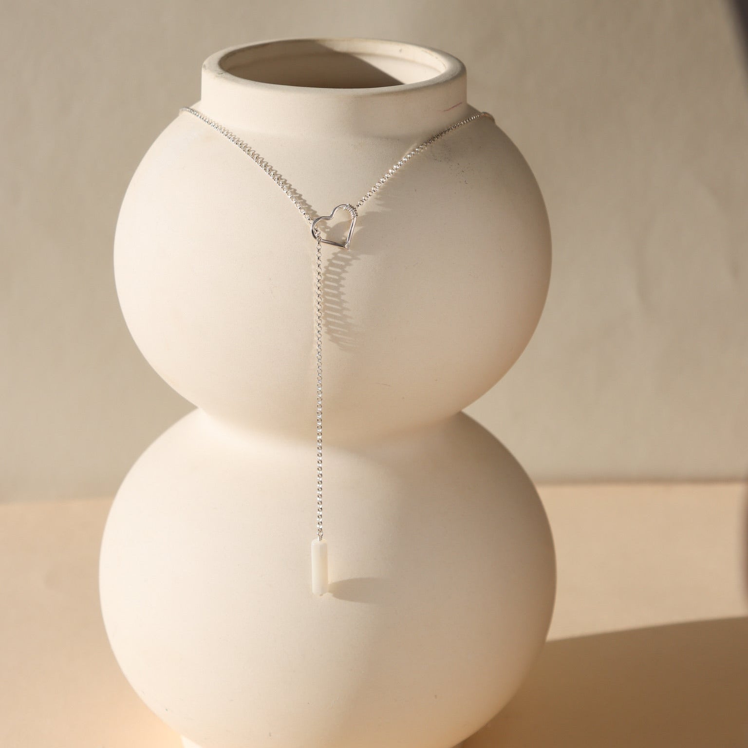 sterling silver lariat necklace with mother of pearl bead displayed on a vase