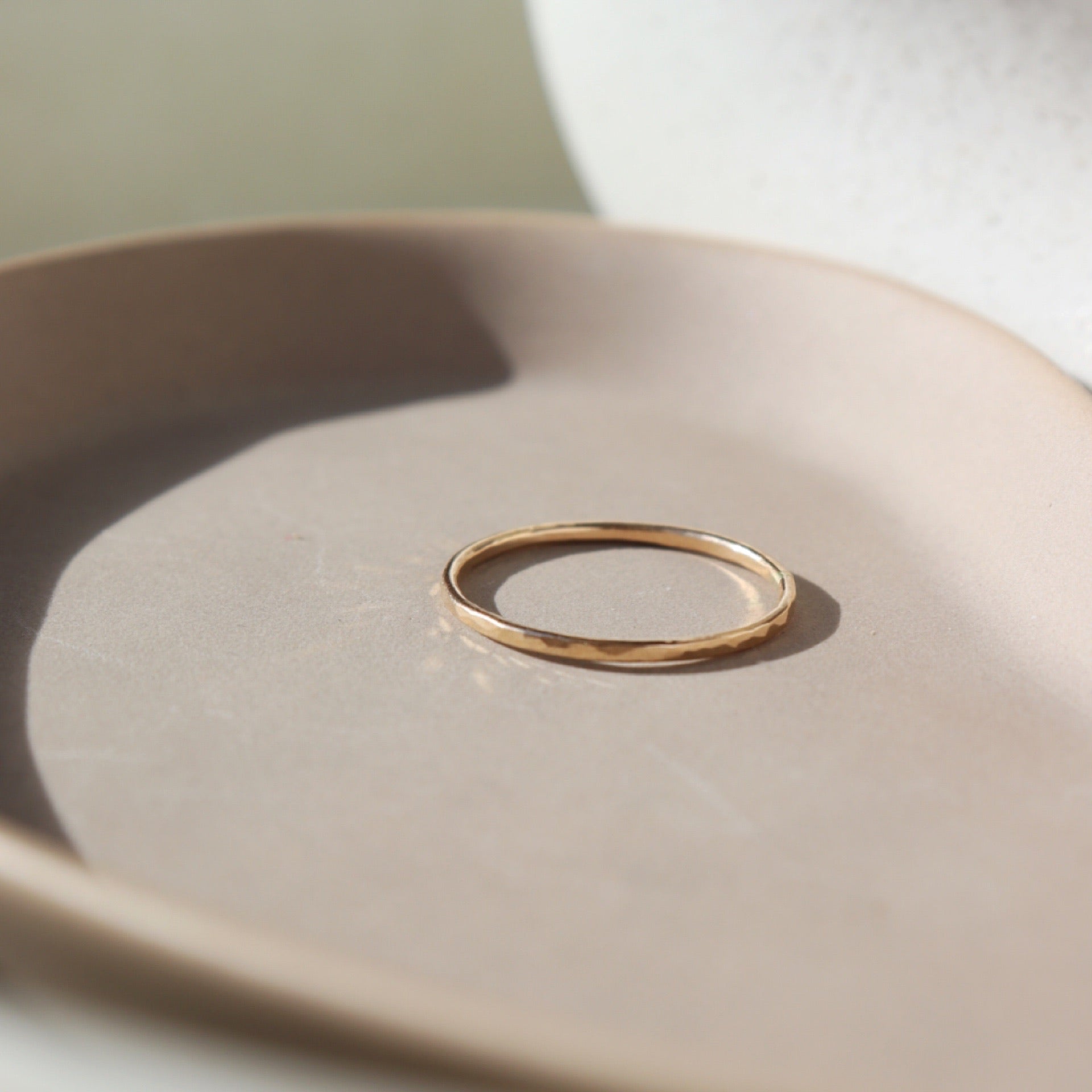 14k gold fill ring placed on a peach colored plate. The plate and ring is placed in the sunlight. This ring features a lightly hammered gold stacking ring, handmade by Token Jewelry in Eau Claire, Wisconsin