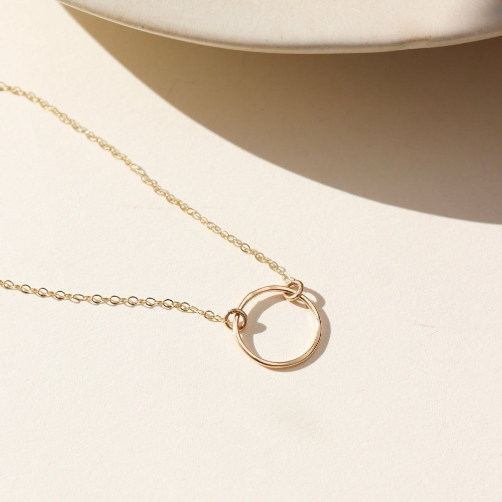 14k gold filled delicate chain necklace with round hammered pendant on a light background