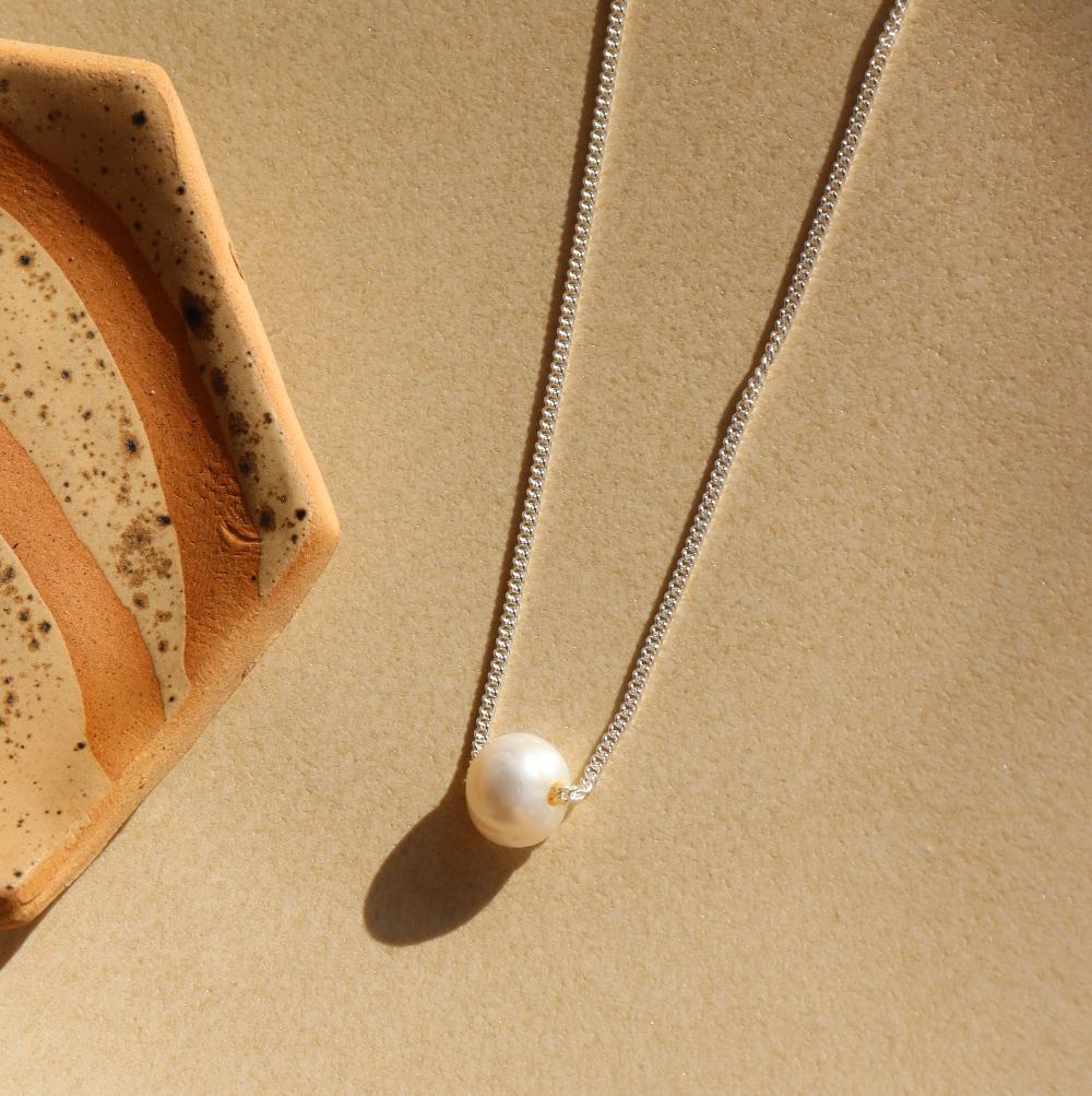 Evelyn Pearl Necklace lad on a tan plate in the sunlight