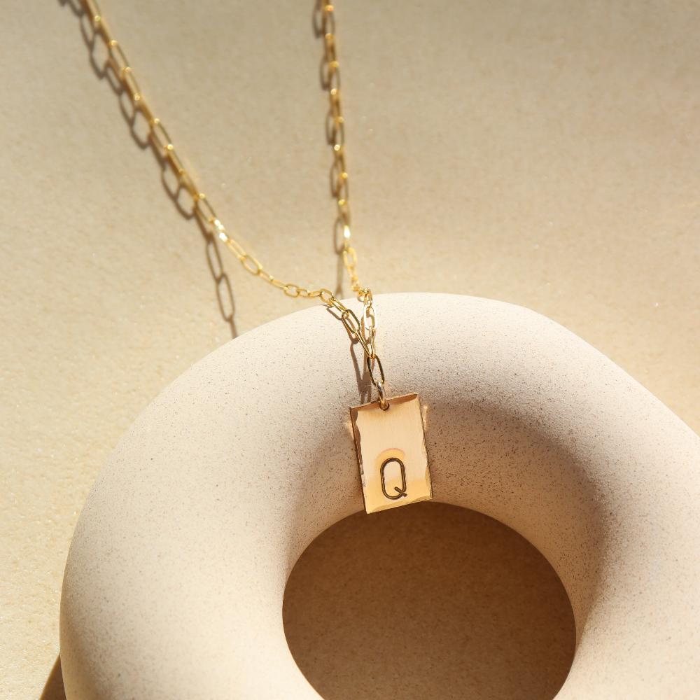 14k gold fill Everly Monogram Necklace on a tan plate in the sunlight