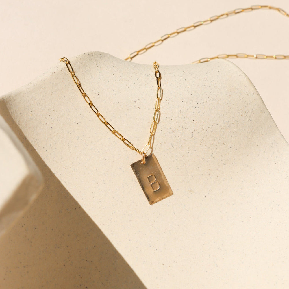 14k gold fill hand stamped pendant on a paperclip chain necklace on a light dish