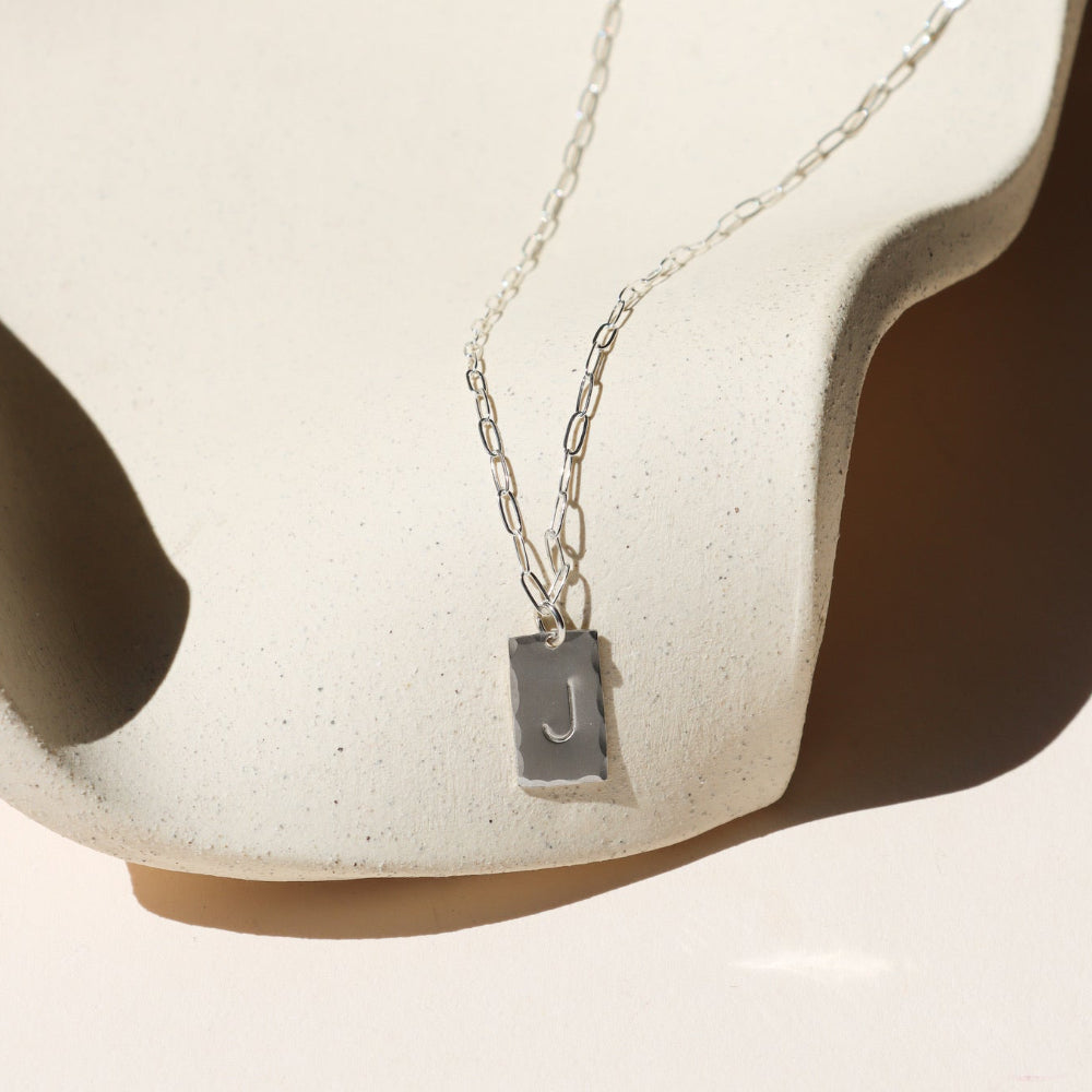 sterling silver hand stamped pendant on a paperclip chain necklace on a light dish