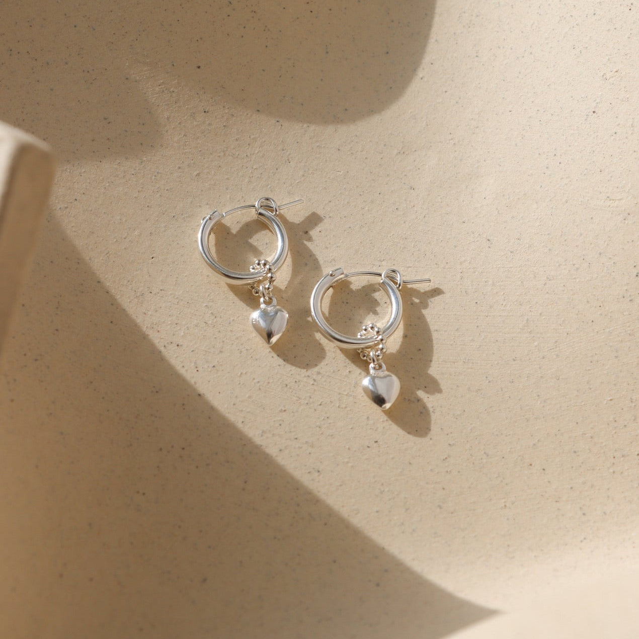 sterling silver heart hoop charms on classic sterling silver hoops laid in the sun