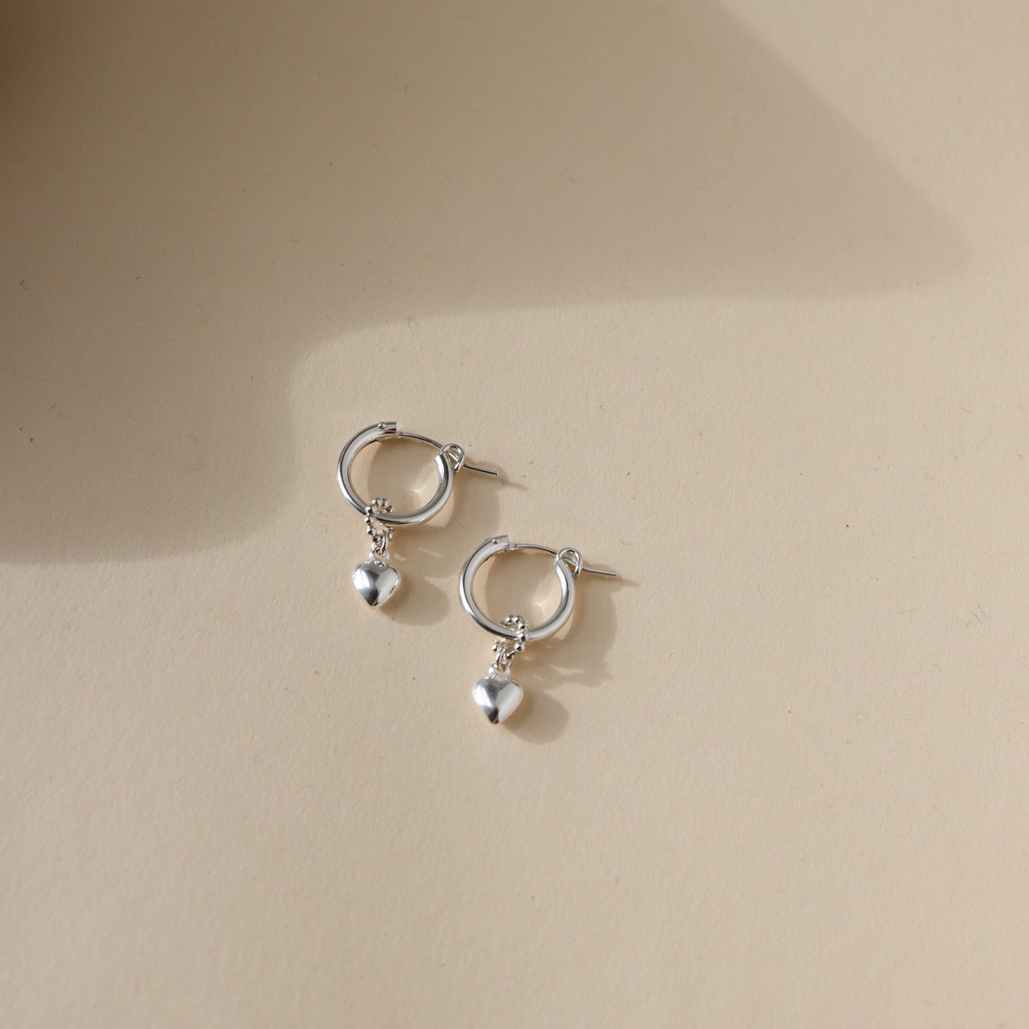 sterling silver heart charm on hoop earrings on light background