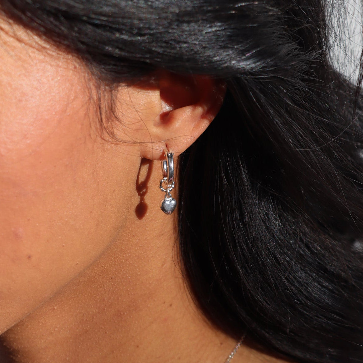 model wearing sterling silver heart charm on classic hoop earring 