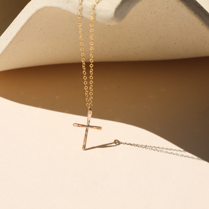 14k gold fill hammered cross pendant on a delicate chain necklace on a light dish