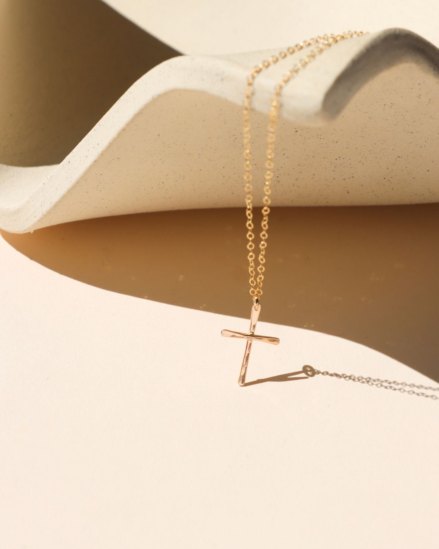 14k gold fill hammered cross pendant on a delicate chain necklace on a light dish