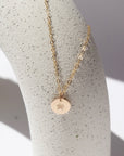 14k Gold fill Children's tiny birth flower charm necklace laid on a white jewelry stand in the sunlight.