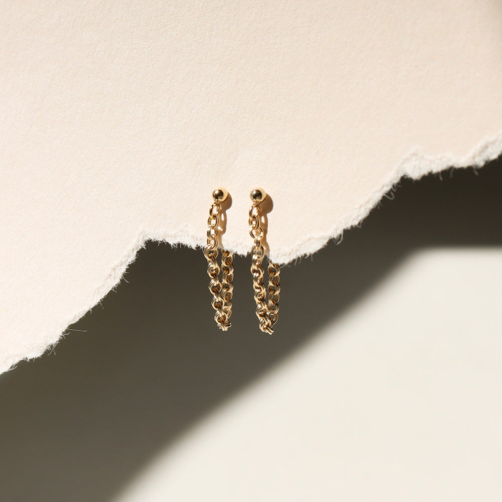 A 14k gold fill textured rolo chain dropped from a classic ball stud, displayed on a cream backdrop in the sunlight. 