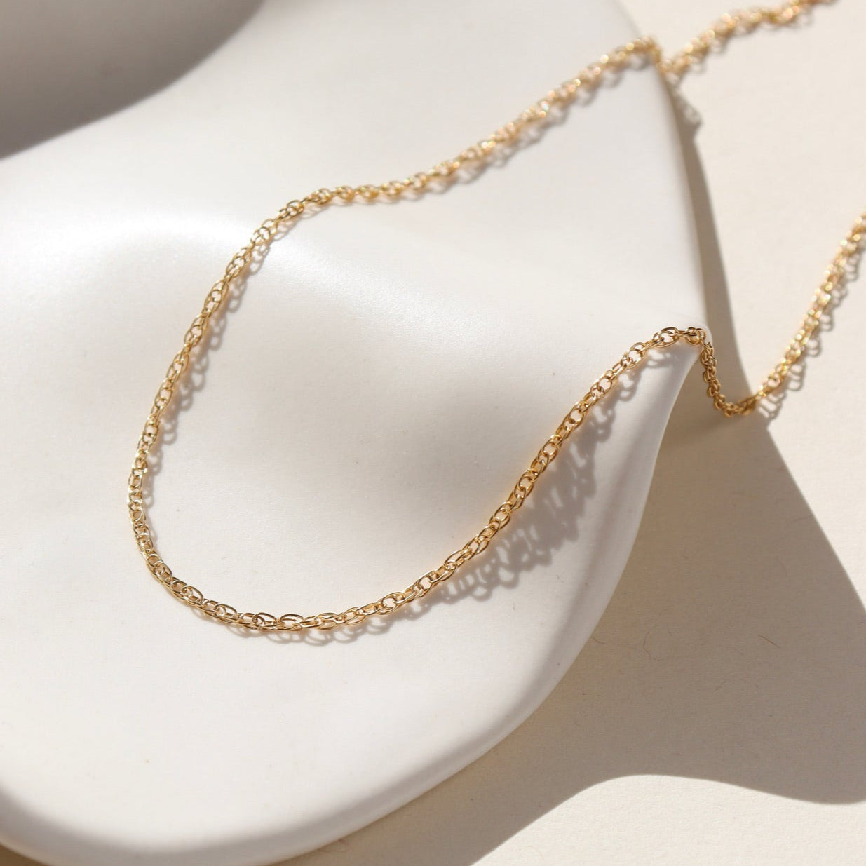 14k gold filled gemma chain laid on a white ceramic dish in the sun.