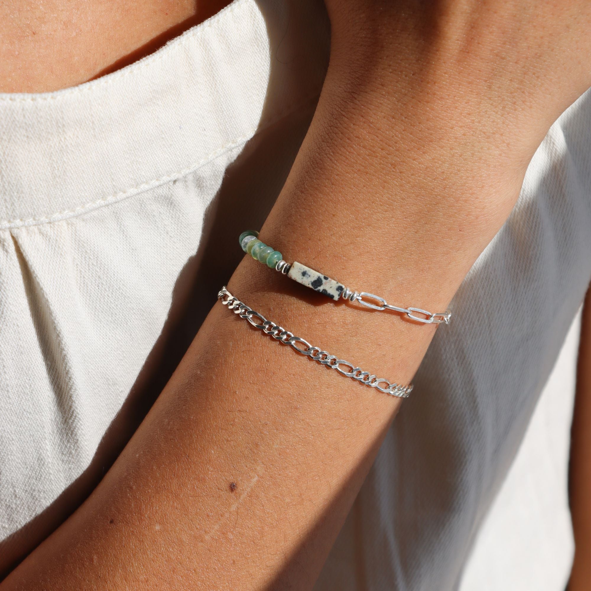 Sterling Silver Figaro Chain Bracelet stacked with a half and half chain and gemstone bracelet on a model