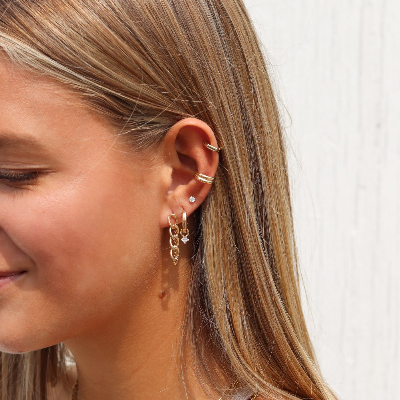 Woman wearing layered gold necklaces, gold hoop and chain earrings, a diamond stud, and gold ear cuffs.