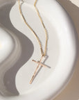 A 14k gold fill thin bar and link chain featuring a 1 1/2" hammered cross pendant. The necklace is displayed on a white dish. 