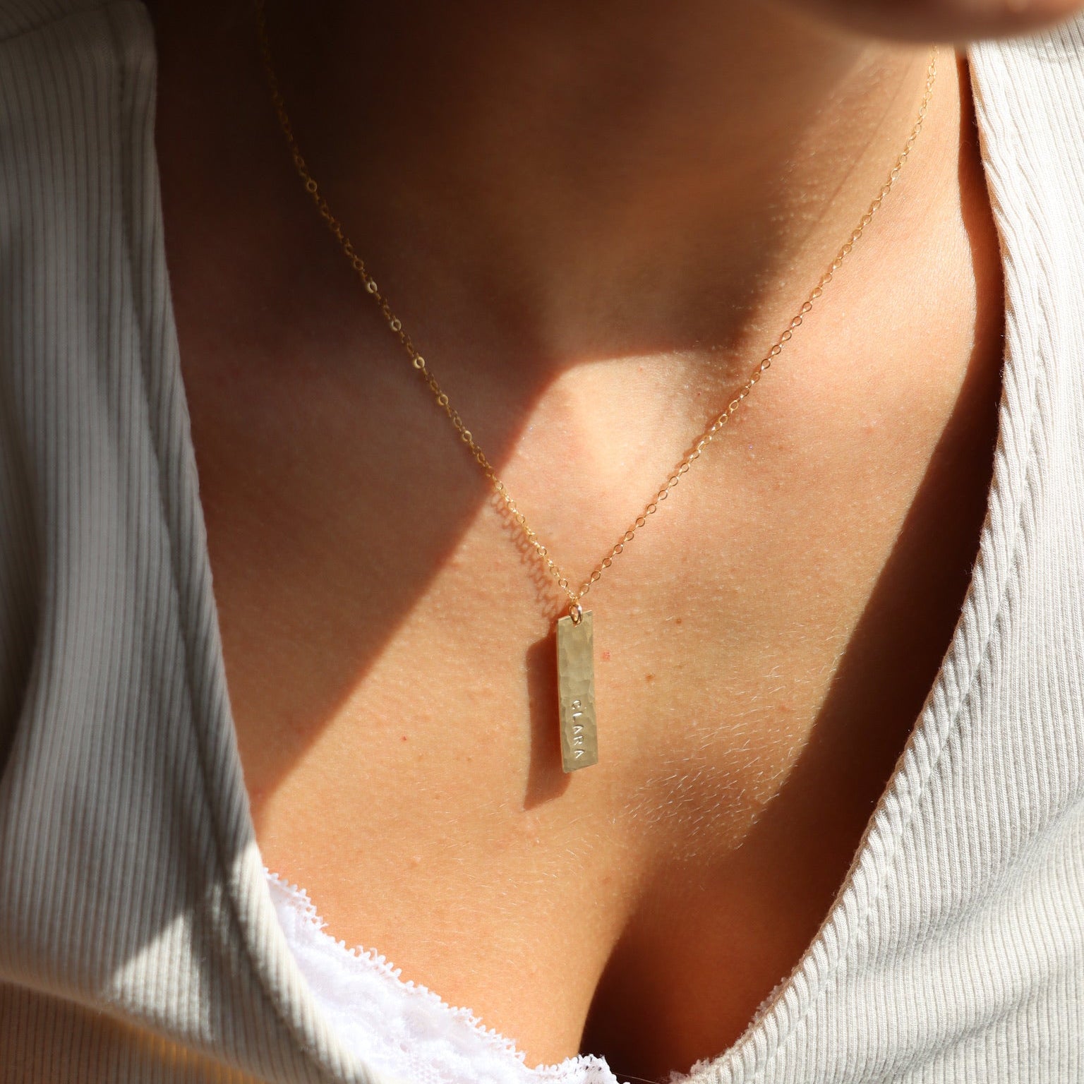 Close-up of a necklace with a pendant on a person wearing a white top.