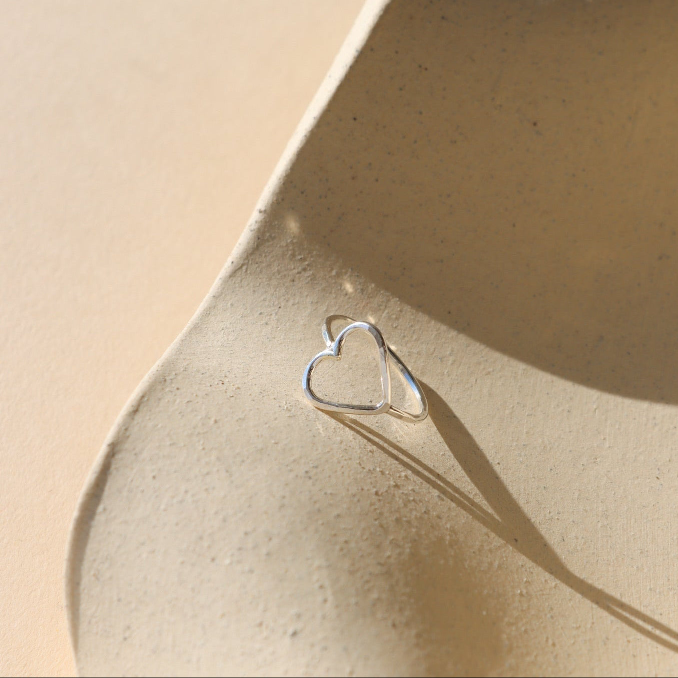 Silver heart-shaped ring on a beige ceramic surface