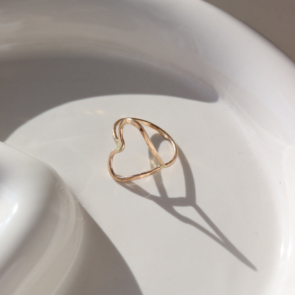 A hammered open heart shaped ring, photographed on a ceramic dish. 