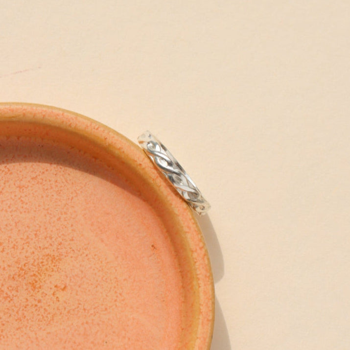 Sterling Silver braided textured ring, displayed on a orange dish