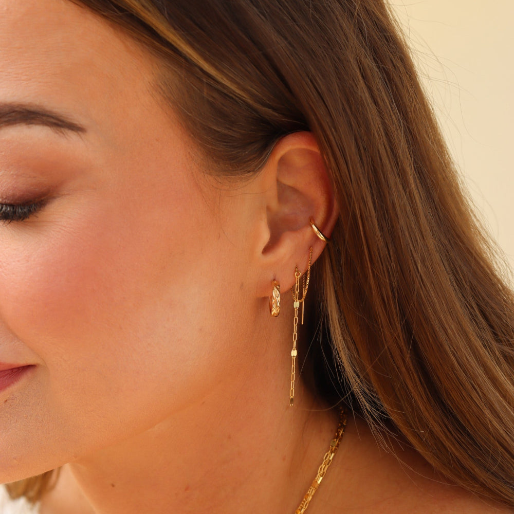 Close-up of a woman wearing gold earrings and necklaces against a neutral background