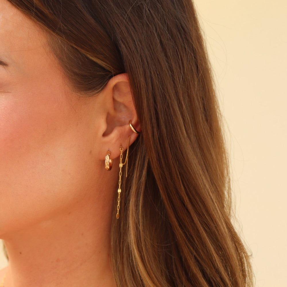 Close-up of a woman wearing gold earrings and necklaces against a neutral background
