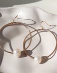 14k gold fill Pearl Hoops laid on a white plate in the sunlight. These earrings feature a hammered hoop with a pearl gemstone connecting the hoop together.