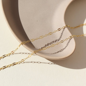 14k gold fill Sylvie chain laid on a tan plate in the sunlight.The dainty Sylvie Chain is the perfect addition to your necklace stack this spring. Wear it on spring break, your winter vacay, or everyday.