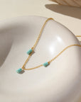 A simple 14k gold fill chain adorned with three charms of stacked turquoise stones, laid out on a cream colored ceramic dish