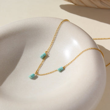 A simple 14k gold fill chain adorned with three charms of stacked turquoise stones, laid out on a cream colored ceramic dish