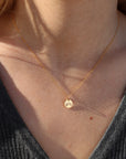 Close-up of a person wearing a delicate gold necklace with a small hand stamped rainbow pendant.