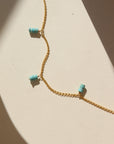 A simple 14k gold fill chain adorned with three charms of stacked turquoise stones, laid out on a cream colored backdrop