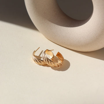 14k gold fill hoop earrings featuring a wave texture, photographed on a sunny table next to a ceramic dish on a white backdrop