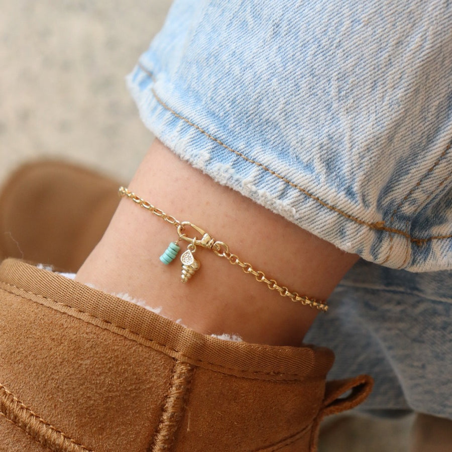 14k gold fill anklet with a swivel push-gate clasp holding a seashell charm and a turquoise charm, photographed on a model wearing brown ugg boots and light wash jeans