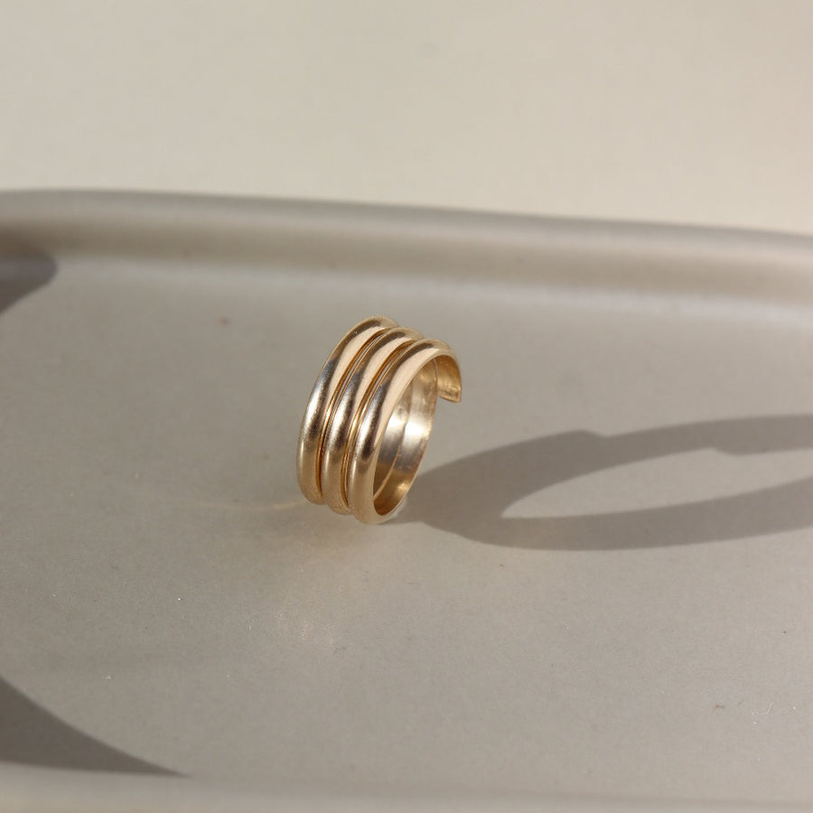 14k gold fill Trinity ring spirals into three bands, photographed on a ceramic dish. This ring features the look of the three layered band look but its only one ring.
