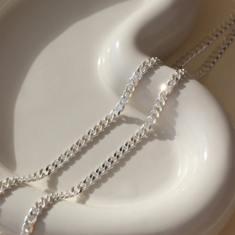 925 sterling silver cuban style chain link bracelet, laid out on a curvy ceramic dish