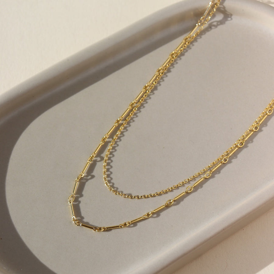a 14k gold fill necklace made up of two chains, laid out on a sunny table