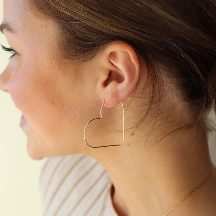 handmade 14k gold fill slide earrings in a heart shape, photographed on a smiling model