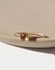 14k gold fill Gaia Ring laid on a tan plate in the sunlight. This ring features a Spiral band with a zircon gemstone. 