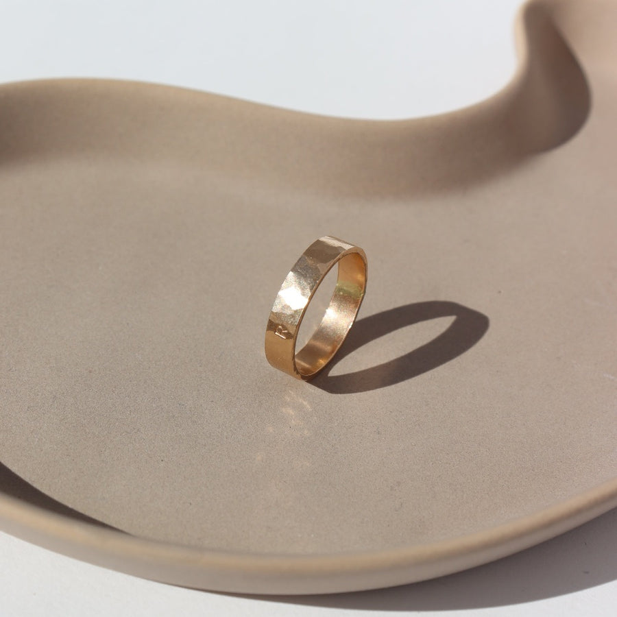 14k gold fill Initial stamped ring laid on a white plate in the sunlight. This ring features a hammered band that you get to customize with name or initials of your choice.